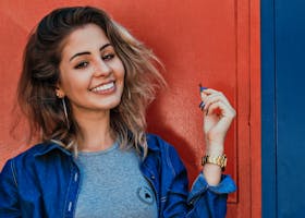 A woman in a denim jacket smiling brightly against a vibrant red and blue background.